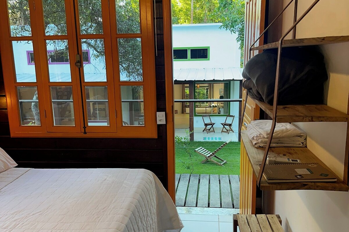 Ein Schlafzimmer mit einem Bett, einer hölzernen Bank und Blick auf einen Außenbereich mit Tisch und Stühlen.