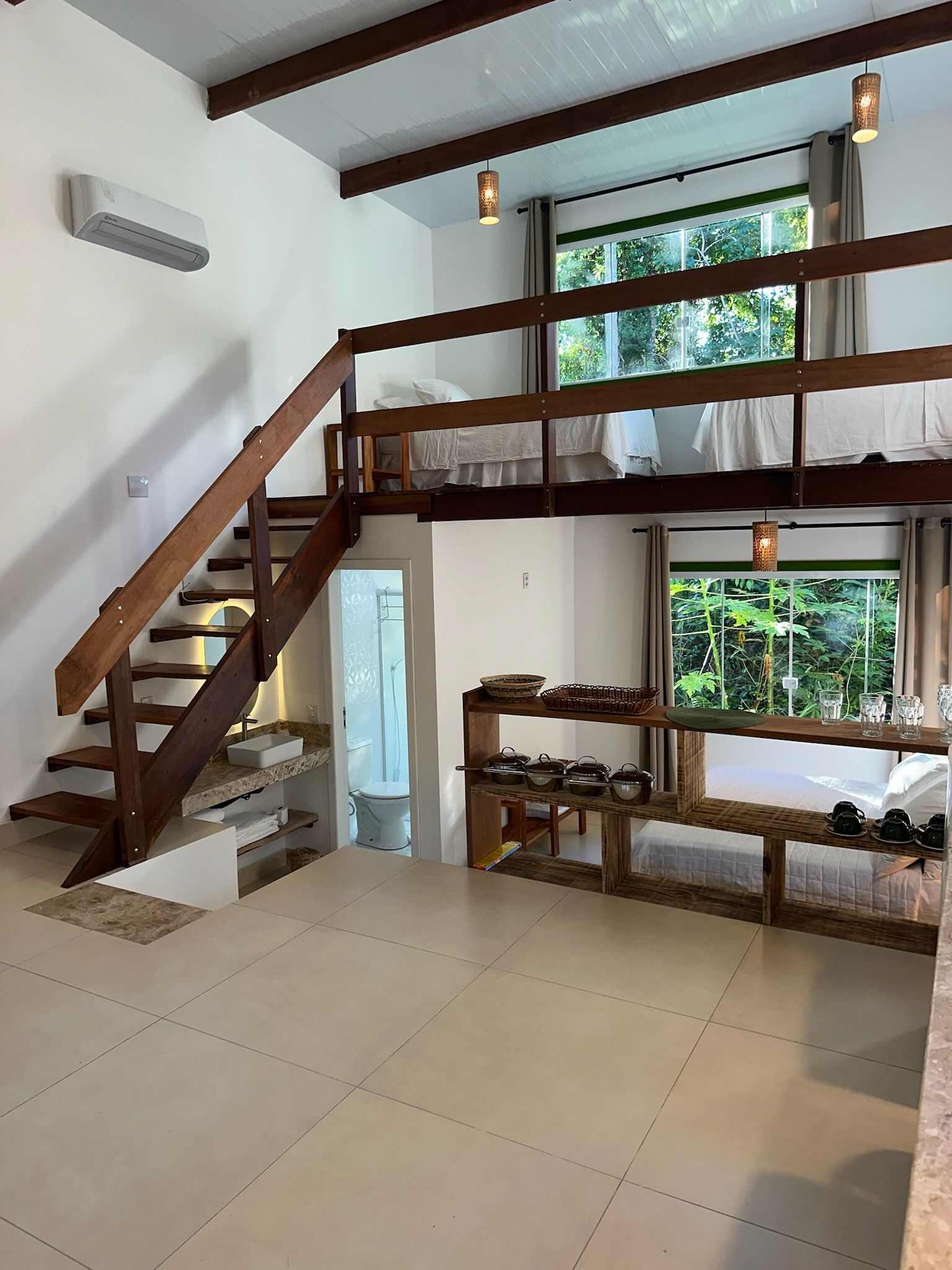 Ein Zimmer mit einer Holztreppe, einem Fenster mit Blick auf Grünflächen, einem Regal mit Küchenutensilien und einer weißen Toilette.
