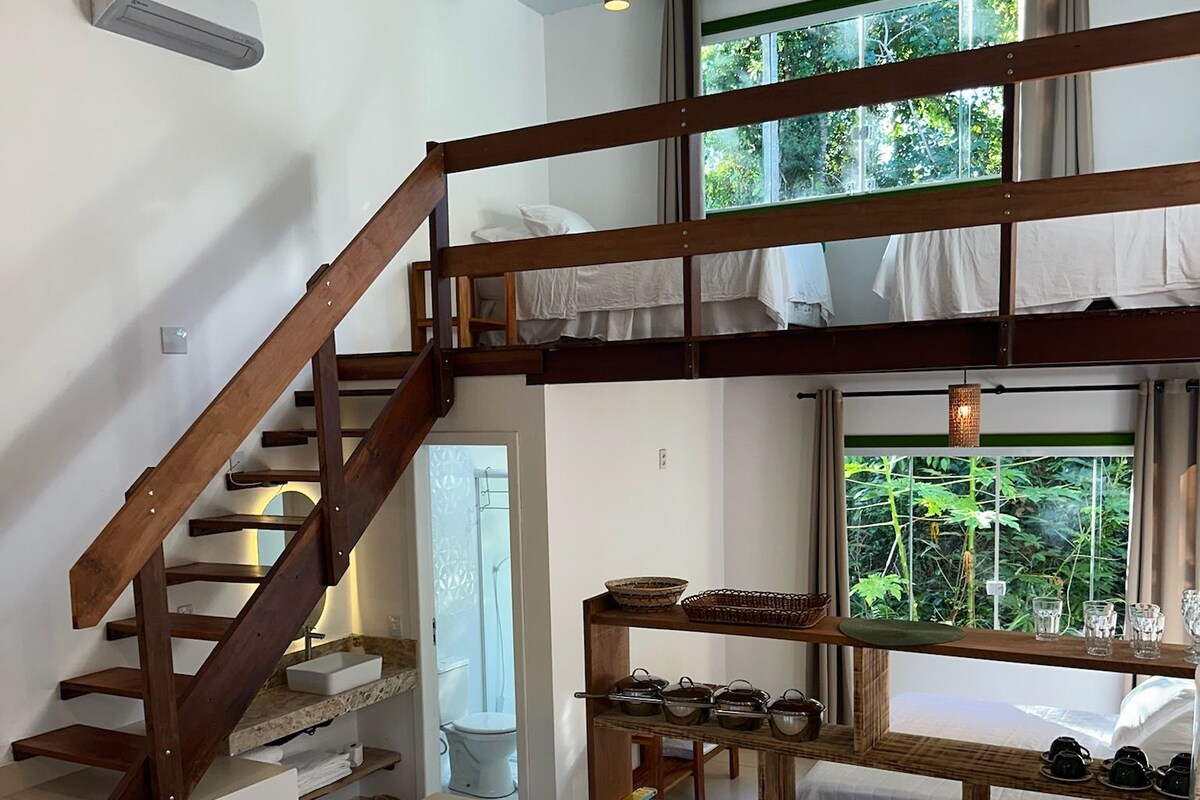 Ein Zimmer mit einer Holztreppe, einem Fenster mit Blick auf Grünflächen, einem Regal mit Küchenutensilien und einer weißen Toilette.