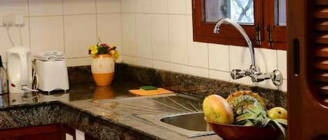 A kitchen with a granite countertop, a sink, a window with a view, and a bowl of fruit.