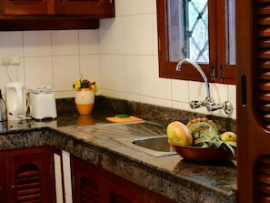 Une cuisine dotée d’un plan de travail en granit, d’un évier, d’une fenêtre offrant une belle vue et d’un saladier rempli de fruits.