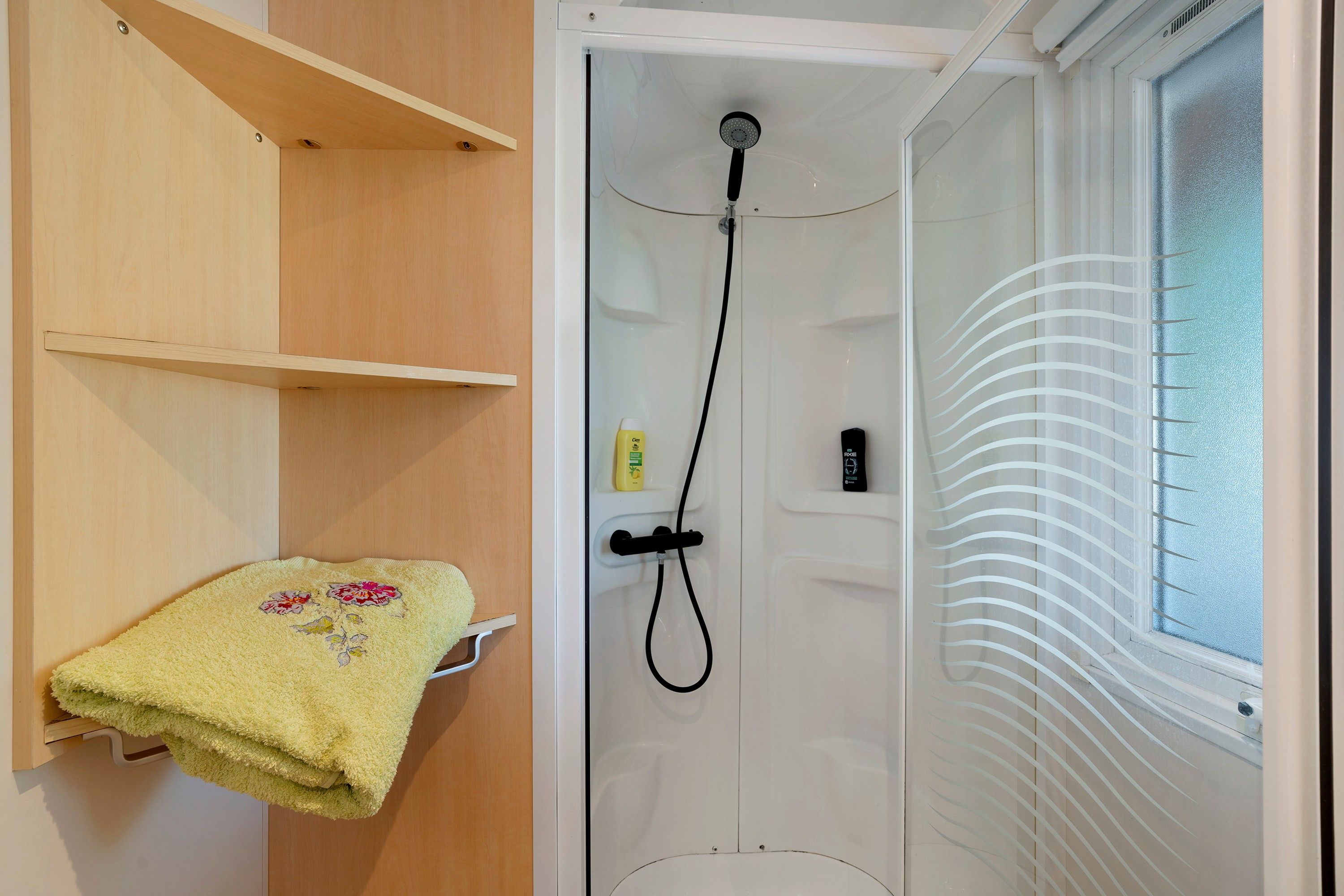 A shower with a handheld showerhead, a towel rack with a towel, and a window with frosted glass.