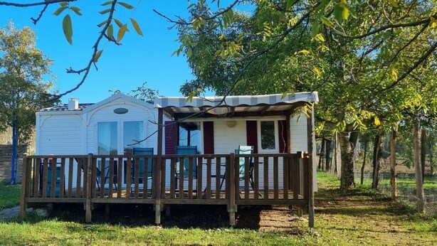 Uma cabana pequena com varanda, quintal cercado e árvores ao fundo.