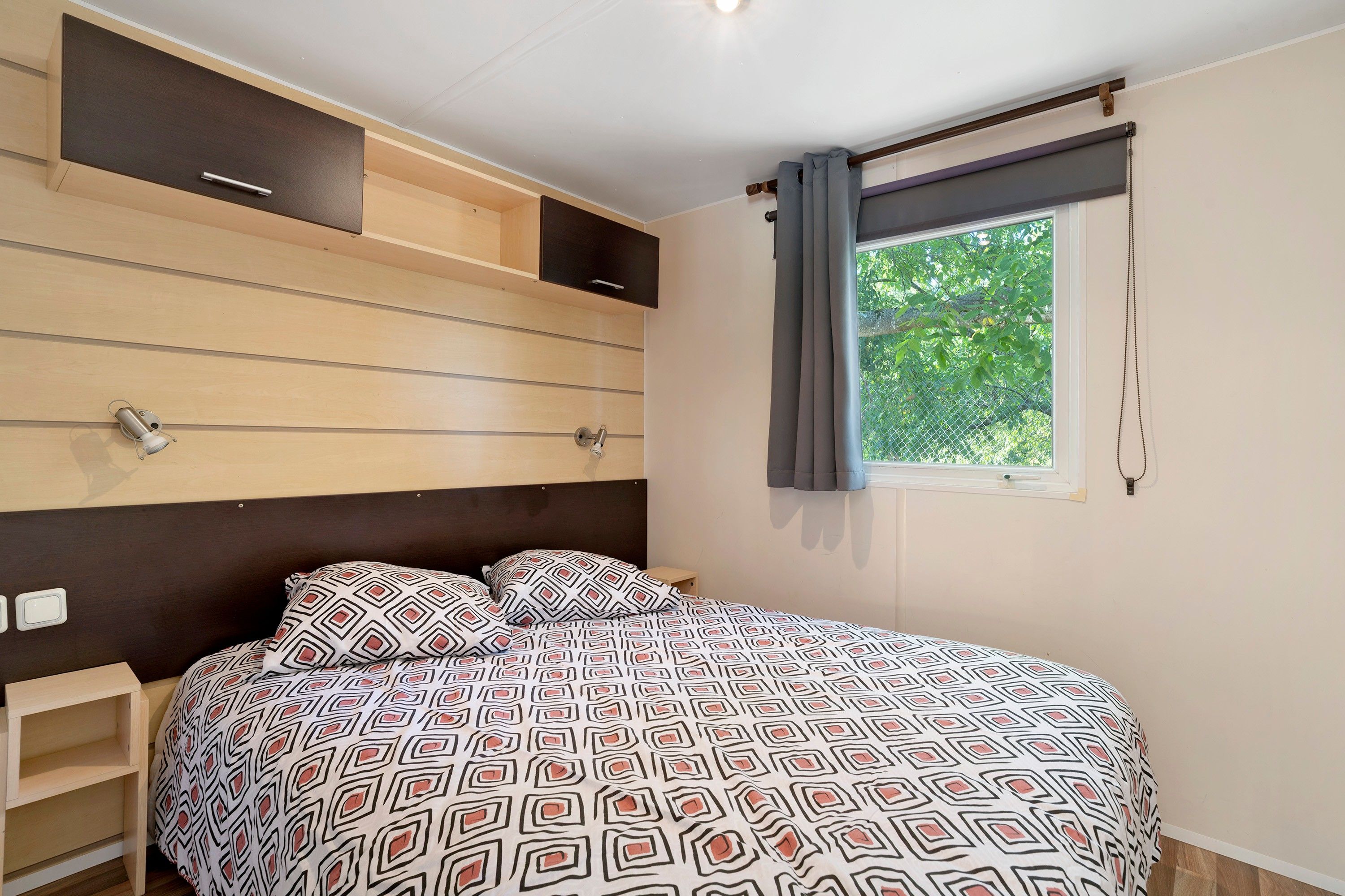 Ein Schlafzimmer mit Bett, Nachttisch, einem Fenster mit Vorhängen und eingebauten Stauraum.