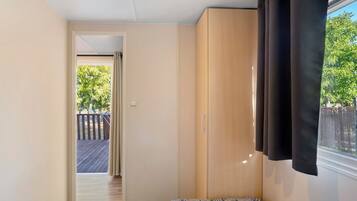Un dormitorio con un armario de madera, una ventana con cortinas y vistas a una terraza y árboles.
