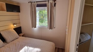 Quarto com cama, mesa de cabeceira, janela com cortinas e prateleira com toalha.