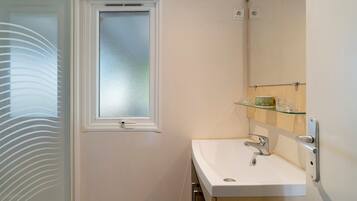 Un baño con un lavamanos blanco, un estante de vidrio encima y una ventana esmerilada, además de una puerta con un panel de vidrio satinado.