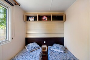 Une petite pièce avec deux lits, une étagère remplie de livres et une fenêtre.