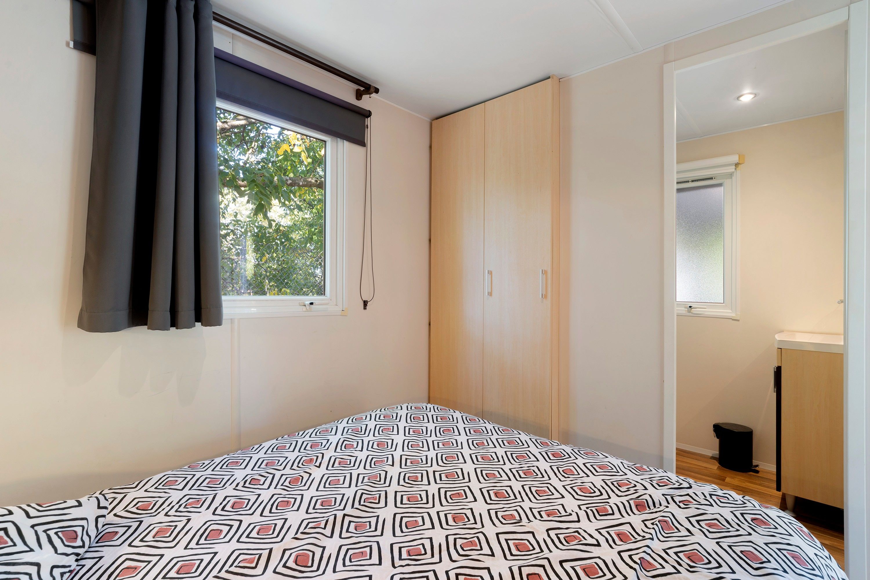 Un dormitorio con cama, armario, ventana con cortinas y vista a árboles.