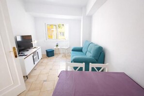Ein gemütlicher Raum mit Fernseher, einem türkisblauen Sofa, einem kleinen Tisch und einer violetten Tagesdecke.
