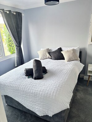 A neatly made bed with a white quilt, grey pillows, and rolled towels. - Newly refurbished 4BR house w/Downstairs ensuite (Sleaford)