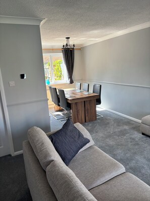A modern living room with a grey carpet, a sofa with patterned cushions, a wooden dining table with chairs, and a chandelier. - Newly refurbished 4BR house w/Downstairs ensuite (Sleaford)