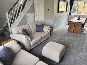 A living room with a grey carpet, a beige sofa with blue cushions, a wooden coffee table, and a staircase. - Newly refurbished 4BR house w/Downstairs ensuite (Sleaford)