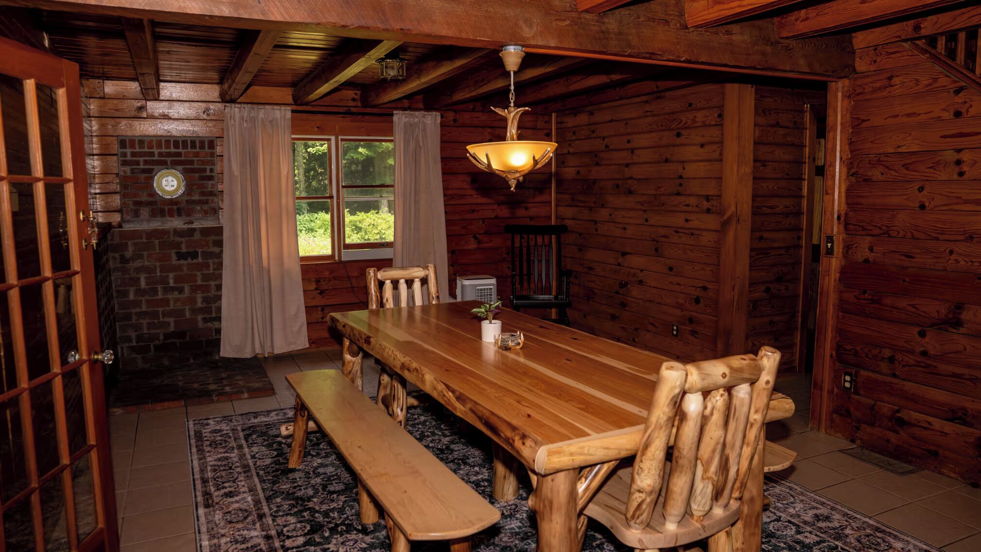 Une salle à manger en bois avec une grande table, des bancs et un lustre.