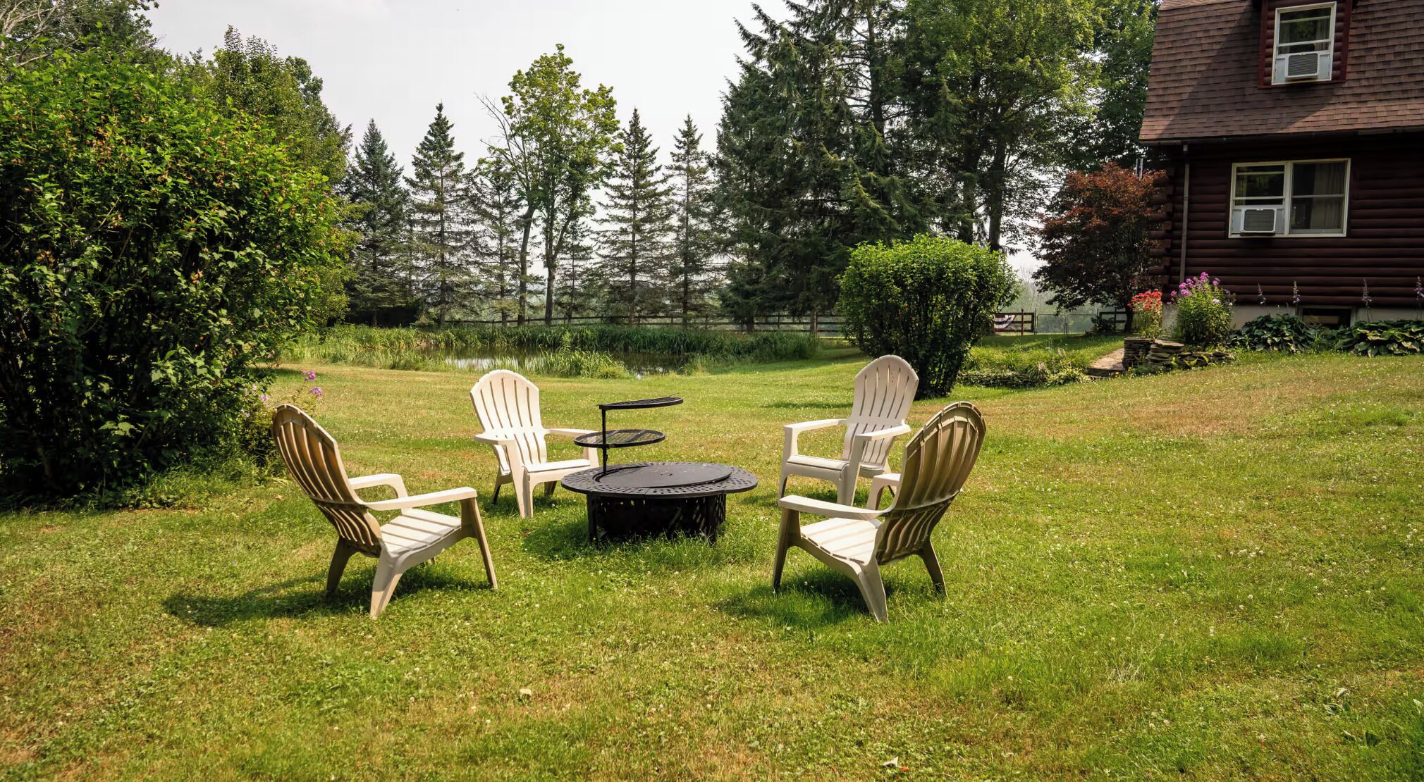 Un espace extérieur aménagé avec une pelouse, comprenant quatre fauteuils Adirondack et une table ronde.