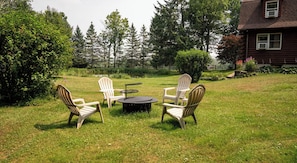 A grassy outdoor seating area with four Adirondack chairs and a round table.