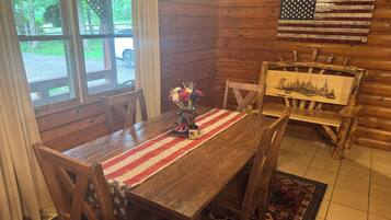 Un coin repas en bois avec une table dressée pour deux personnes, un drapeau accroché au mur et une vue sur l’extérieur.