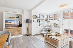 Uma sala de estar moderna com televisão de tela plana, um sofá, uma mesa de centro e uma janela grande com vista.