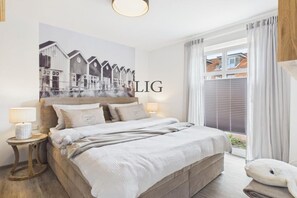 Ein Schlafzimmer mit einem großen Bett, zwei Nachttischen, einem Wandbild und einem Fenster mit Vorhängen.