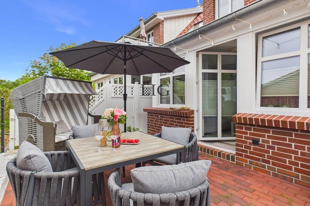 Une terrasse extérieure avec une table et des chaises, un barbecue et un grand parasol.