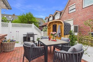 A patio with a table and chairs, a barbecue grill, and a wooden door. - Holiday apartment Norderloog 2 (Langeoog)
