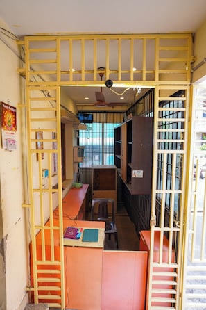 A narrow corridor with yellow railings, a ceiling fan, and a window with bars. - Vel Ohm Homestay (Puducherry)