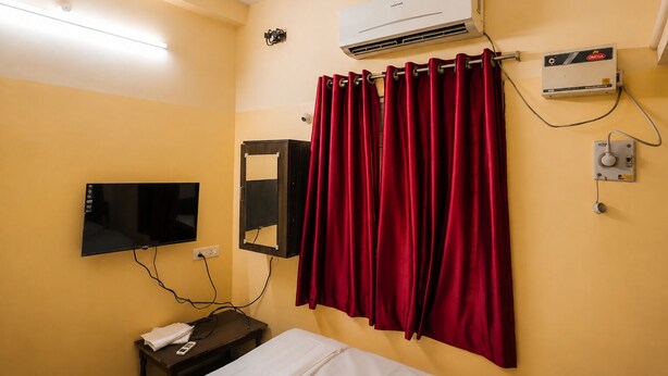 A hotel room with a bed, a TV, an air conditioning unit, and a ceiling fan. - Vel Ohm Homestay (Puducherry)