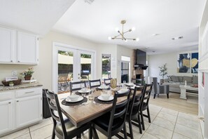 A modern kitchen with white cabinets, a dining table set for six, and a view of the backyard through large windows. - Pool Haven | Hot Tub Fire Pit Game Room Sleeps 18 (San Antonio)