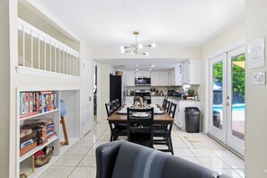 A modern kitchen with white cabinets, a dining area with a wooden table and chairs, and a view of a swimming pool through the glass door. - Pool Haven | Hot Tub Fire Pit Game Room Sleeps 18 (San Antonio)