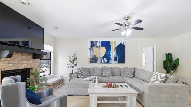 Ein modernes Wohnzimmer mit einem Ecksofa, einem Kamin, einem Deckenventilator und abstrakter Wandkunst.