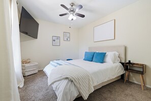 Ein Schlafzimmer mit einem Bett, einem Deckenventilator, einem Nachttisch und einem an der Wand hängenden Bild.