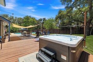 Ein Garten mit Whirlpool, Holzterrasse, Pool und Gartenmöbeln.