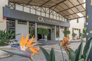 Ein Gebäude mit einem Schild, auf dem 'CA CLUB AMARILIS' steht, und einem überdachten Eingang. Sichtbar sind Kübelpflanzen und ein klarer Himmel.