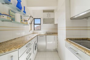 Eine kompakte Küche mit weißen Schränken, einer integrierten Waschmaschine und einer Arbeitsplatte aus Granit.