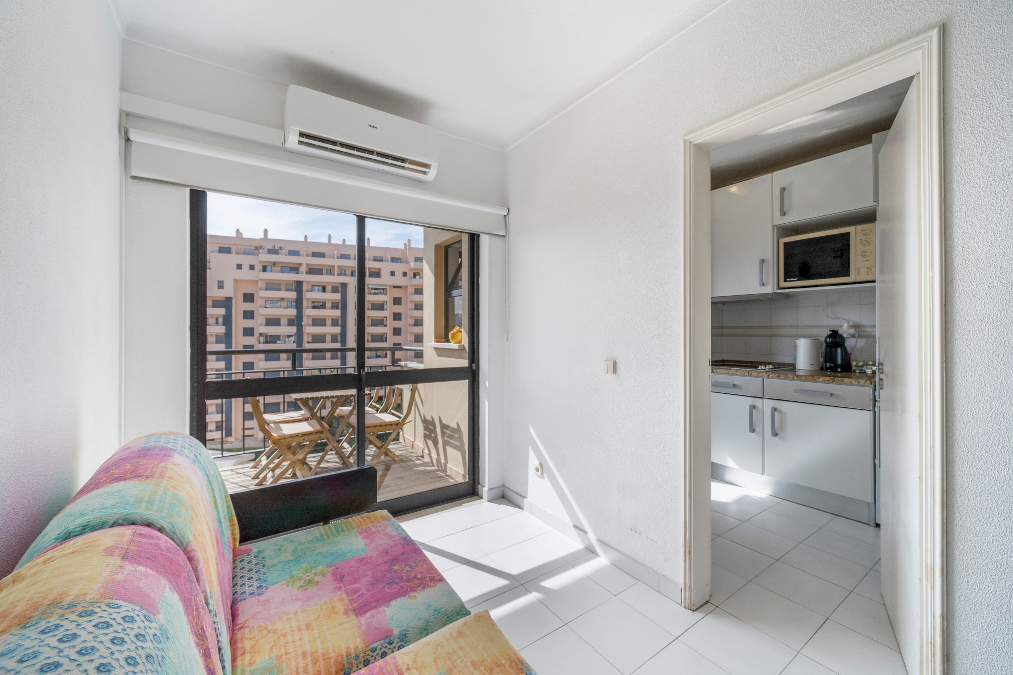 A modern apartment with a balcony, a kitchenette, and a colorful sofa.