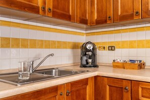 Eine Küche mit Holzausstattung, einer Edelstahlspüle, einer Kaffeemaschine und einer gefliesten Spritzschutzwand.