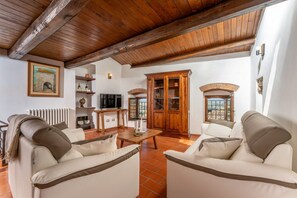 Una sala de estar con chimenea, vigas de madera en el techo, un televisor y un mueble grande.