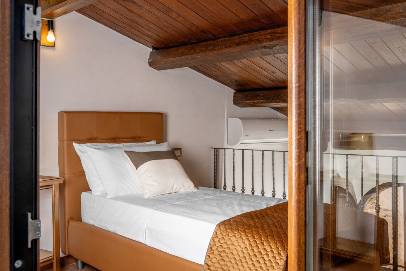 A single bed with a headboard, white bedding, and a wooden ceiling.
