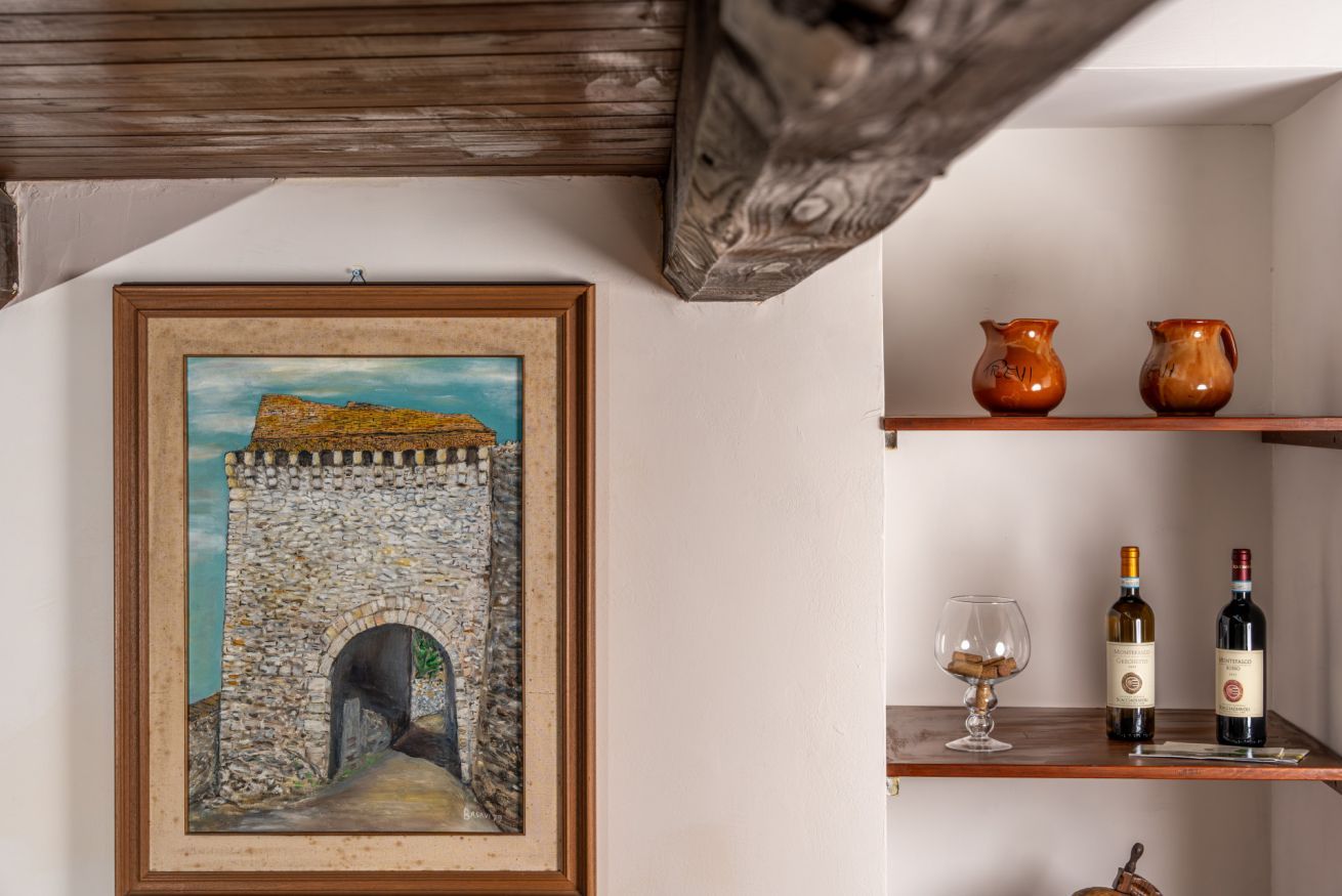 A framed painting of a stone archway, wooden shelves with pottery and wine bottles, and a rustic ceiling beam.