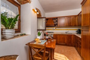 Eine Küche mit Holzausstattung, gefliestem Spritzschutz, einem Fenster mit Pflanzen und einem Esstisch mit Stühlen.