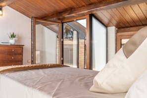 Een slaapkamer met een bed, houten plafond en een schuifdeur naar buiten.