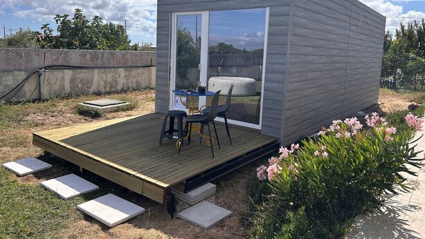 A small, modern outdoor structure with a wooden deck, a table, and chairs. - Tiny House with Shared Pool, Wi-Fi, and Air Conditioning (Palmela)