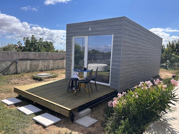 A small, modern outdoor structure with a wooden deck, a table, and chairs. - Tiny House with Shared Pool, Wi-Fi, and Air Conditioning (Palmela)