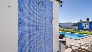 Ein Poolbereich mit einer blauen Fliesenwand, einer weißen Wand mit einer Dusche und einem wolkenlosen Himmel.