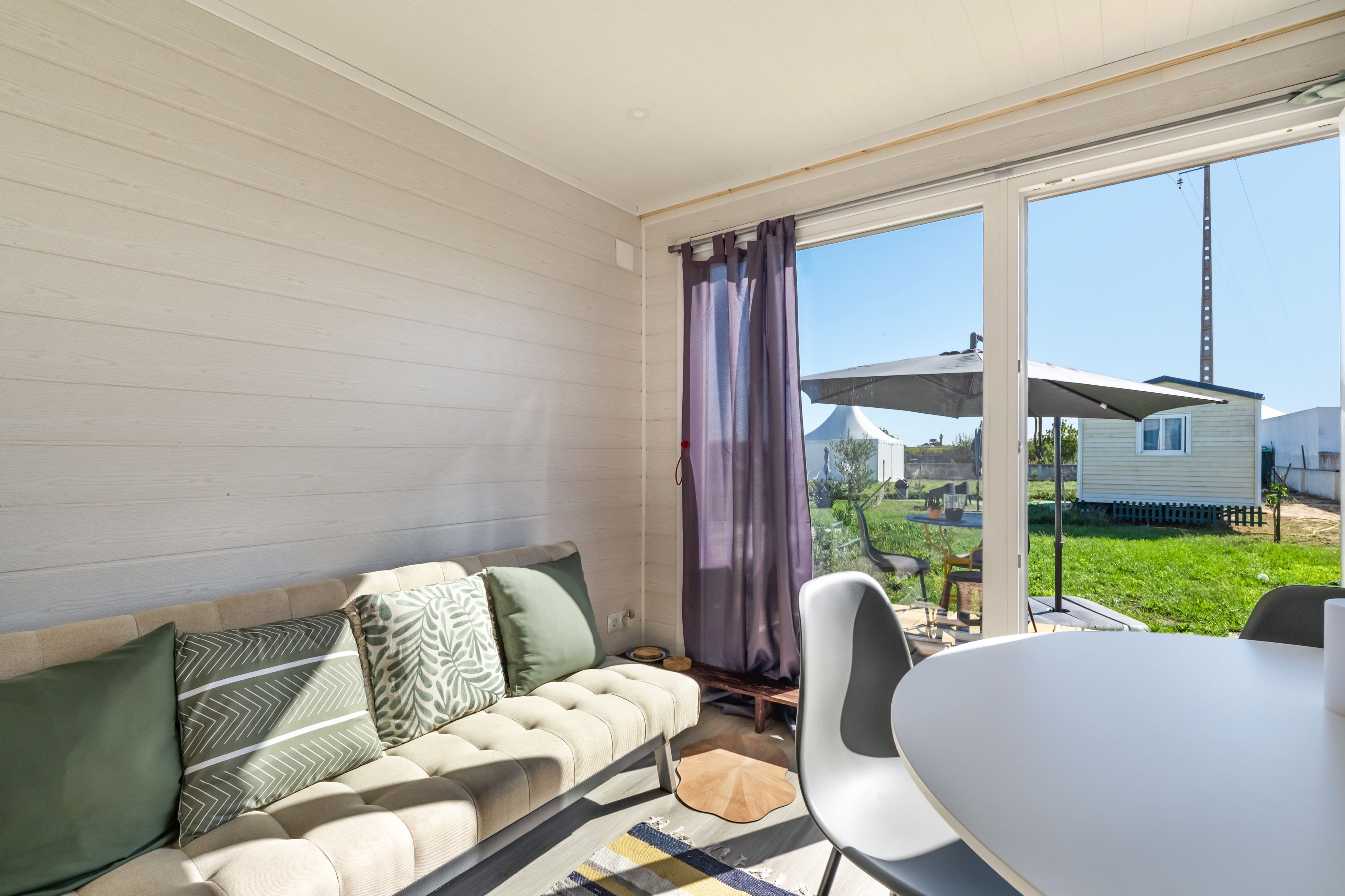 Un salon moderne avec un canapé, une table à manger et une vue sur un jardin et les maisons voisines.