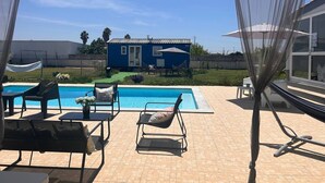 A poolside area with lounge chairs, a small house in the background, and a clear sky. - Tiny House with Shared Pool, Wi-Fi, and Air Conditioning (Palmela)