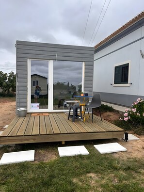 A covered outdoor area with a table and chairs, a window, and a view of a house. - Tiny House with Shared Pool, Wi-Fi, and Air Conditioning (Palmela)
