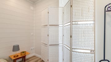 A room with a white partition, a small wooden table with a lamp, and a bed with a floral bedspread.