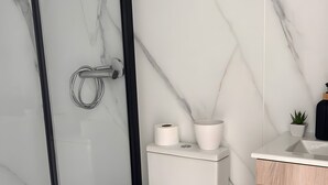 A modern bathroom with a toilet, a glass shower enclosure, a sink, and a small trash bin. - Tiny House with Shared Pool, Wi-Fi, and Air Conditioning (Palmela)