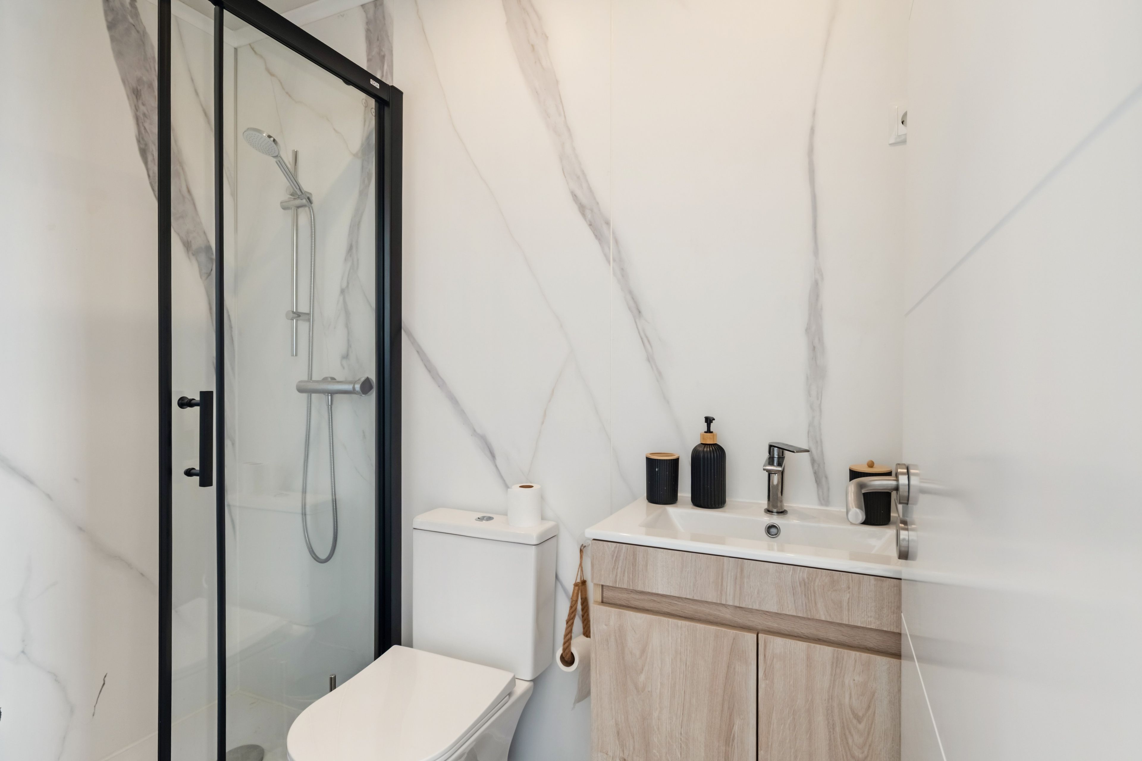 A modern bathroom with a glass-enclosed shower, a toilet, and a vanity with a sink and soap dispenser.